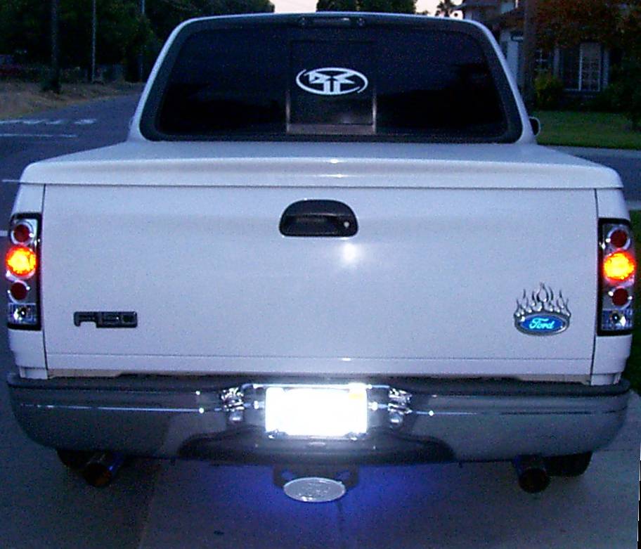 Rear view of a white Ford F-150 pickup at dusk with clear tail lights and dual exhaust tips