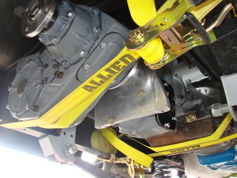 1979 Ford Bronco - The vehicle's drivetrain components are secured with yellow ratchet straps, showing part of the transfer case and transmission.