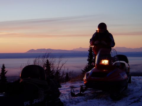 2000 Ford E350 - Two snowmobiles are parked on a snowy ridge as the sun rises over a misty valley.