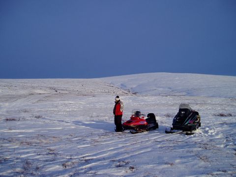 2000 Ford E350 - Two snowmobiles are parked in a wide, open snowy field with a person standing near one of them.