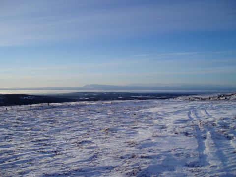 2000 Ford E350 - Tire tracks mark a path through a snow-covered landscape with distant mountains under a bright blue sky.