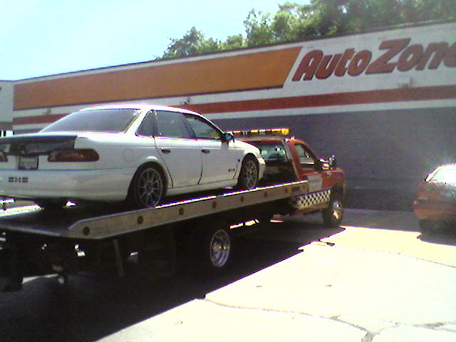 White 1993 Ford Taurus sedan with a rear spoiler on a tow truck