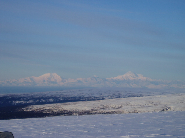 Snowy mountain range under a clear blue sky, with a snow-covered foreground and middle ground