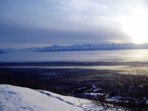 2000 Ford E350 - A vast winter landscape unfolds with snow-covered mountains, a thick layer of fog, and dark forests under a bright, cloudy sky.