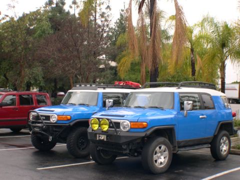 2007 Toyota FJ Cruiser - Two blue 2007 Toyota FJ Cruisers are parked in a lot, with one prominent yellow fog lights on its bumper.