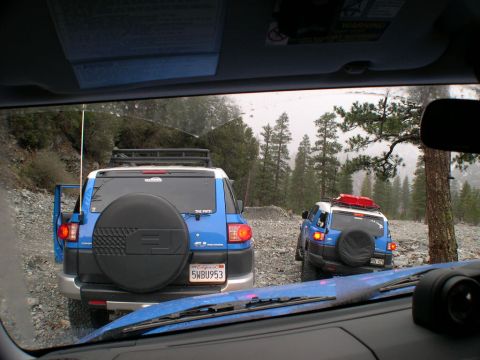 2007 Toyota FJ Cruiser - Two blue Toyota FJ Cruisers navigate a rocky, wooded terrain, with one vehicle's door open.
