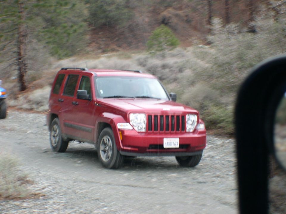 Red Jeep Liberty on a gravel road, front 3/4 view. License plate reads ARD763