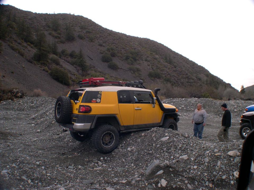 Yellow 2007 Toyota FJ Cruiser on a rocky trail with two people standing nearby