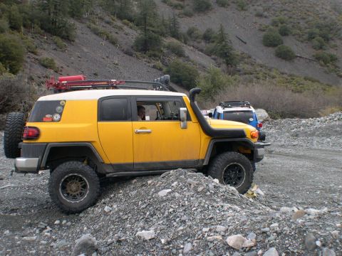2007 Toyota FJ Cruiser - A yellow Toyota FJ Cruiser navigates a rocky terrain with a snorkel and roof rack, followed by another SUV.