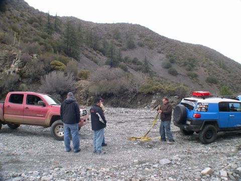 2007 Toyota FJ Cruiser - Two off-road vehicles and several people are gathered in a dry creek bed with a steep, vegetated hillside in the background.