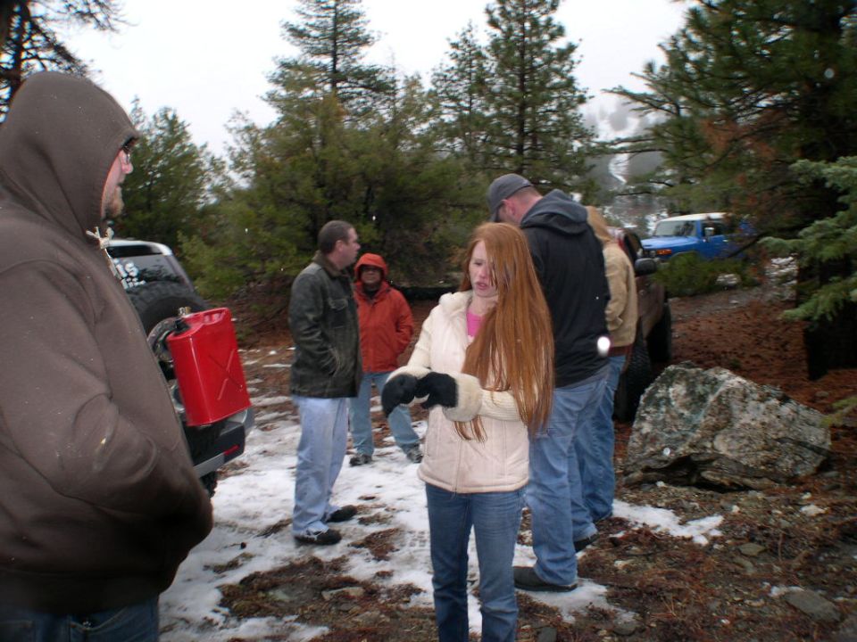 Two Toyota FJ Cruisers, one black and one blue, in a snowy wooded area with people standing around