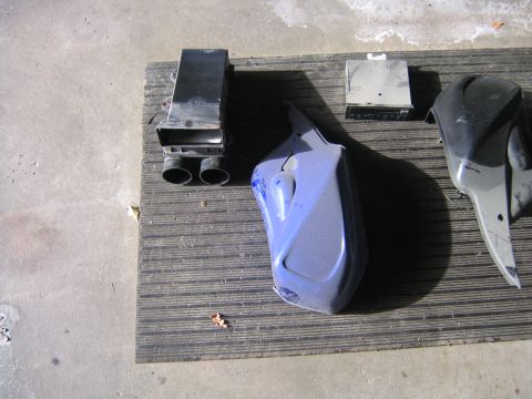 1994 Ford Bronco - Various automotive parts, including an air intake box, a blue fender, and a car stereo, are laid out on a mat.