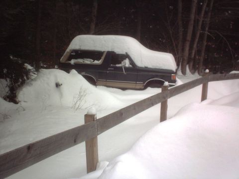 1966 Land Rover Discovery - Ford Bronco with camper shell buried in snow next to a wooden fence.
