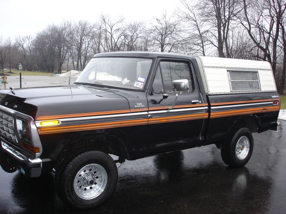 Black 1979 Ford F-150 pickup truck with orange and silver side stripes and a white camper shell