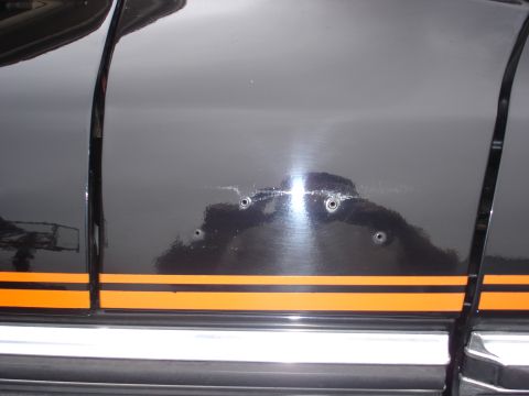 1979 Ford F-150 - Close-up of a 1979 Ford F-150's side panel, showing orange racing stripes and evidence of bullet impacts.