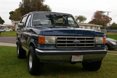 1986 Ford Bronco - This dark blue 1987 Ford Bronco 4x4 is parked on a grassy lawn in front of a residential area.