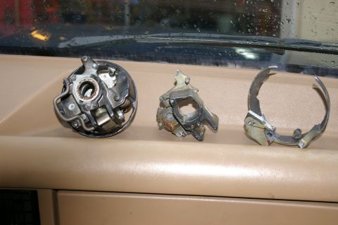 1986 Ford Bronco - Three disassembled parts of a vehicle's ignition system, likely a distributor cap, rotor, and related components, are laid out on a car's d…