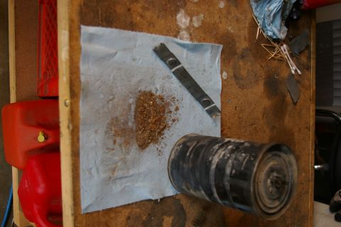 1986 Ford Bronco - A used oil filter sits on a paper towel with debris, next to red gas cans on a workbench.