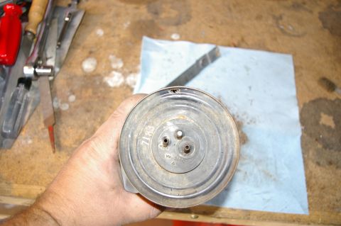 1986 Ford Bronco - A hand holds a metal canister with three ports, resting on a blue paper towel on a workbench.