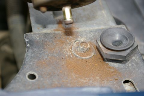 1986 Ford Bronco - Corroded metal bracket with a bolt and washer, indicating wear and tear on a vehicle component.