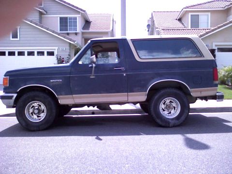 1986 Ford Bronco - Side profile of a 1986 Ford Bronco, showing its two-tone paint scheme and classic SUV body style.