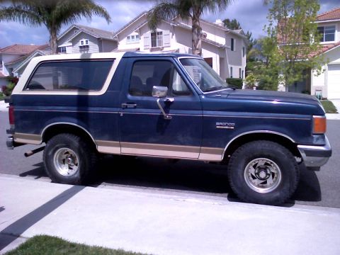1986 Ford Bronco - This 1986 Ford Bronco is seen from the side, its distinctive blue paint, tan stripe, and white removable top.
