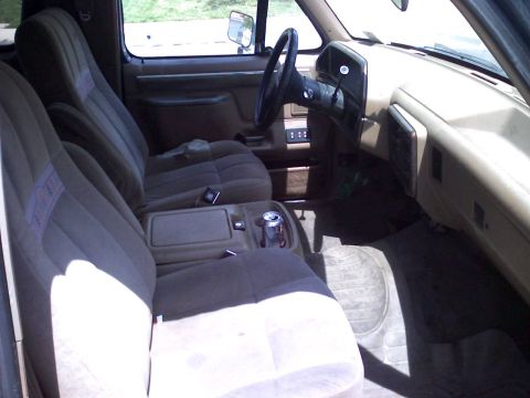 1986 Ford Bronco - The interior of a Ford Bronco features cloth seats and a tan dashboard with a steering wheel and center console.