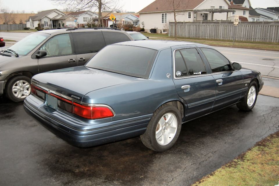 Blue sedan parked next to a minivan. Rear quarter view