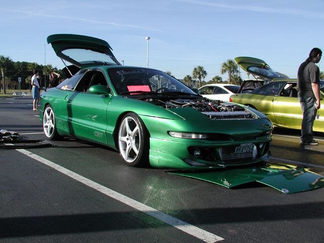 Green 1994 Ford Probe with hood and trunk open, parked next to a yellow car
