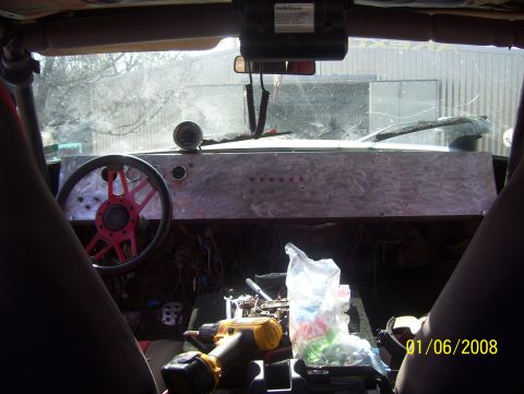 1978 Ford Bronco - The interior of a vehicle shows a custom dashboard with many switches and a bright red steering wheel.