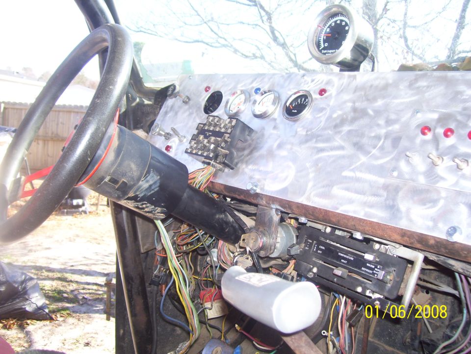 Custom dashboard with aftermarket gauges, fuse box, and exposed wiring. Steering column and HVAC controls are visible