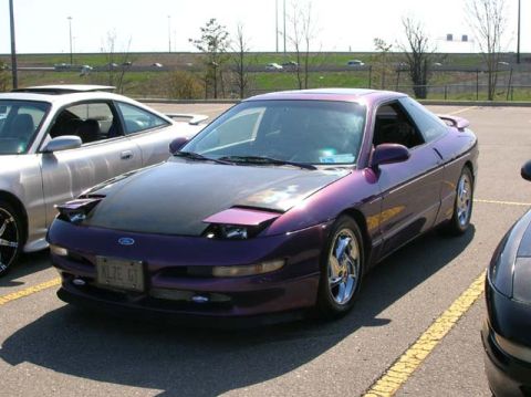 1994 Ford Probe - A purple 1994 Ford Probe is parked in a lot, showing its distinctive pop-up headlights and aftermarket hood.