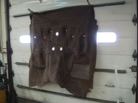 1996 Ford Bronco - Car carpet with holes is hung on a garage door, possibly for drying or inspection.