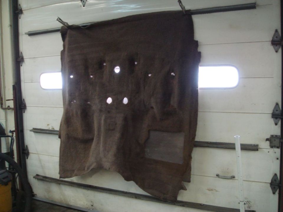 Brown car carpet with multiple holes hanging on a white garage door