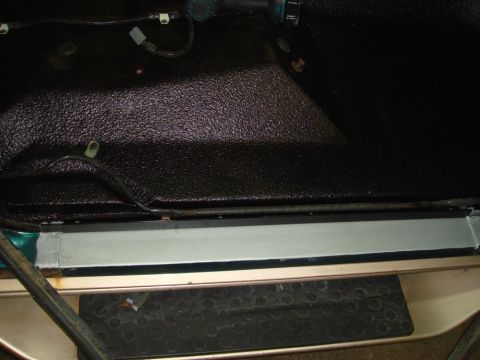 1996 Ford Bronco - The interior floor of a vehicle shows a textured black liner and a silver metal trim piece along the edge.