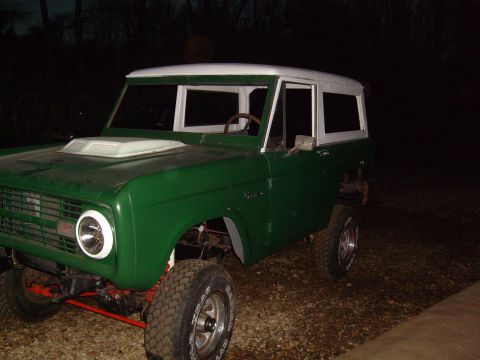 1974 Ford Bronco - This green Ford Bronco with a white top is parked outdoors at night, showing its front and side profile.