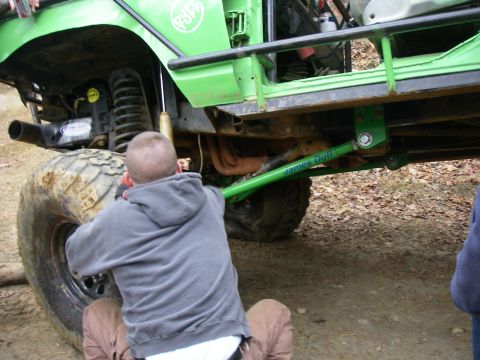 1978 Ford Bronco - A person works on the suspension of a modified off-road vehicle, with "James Duff" branding visible on a green component.
