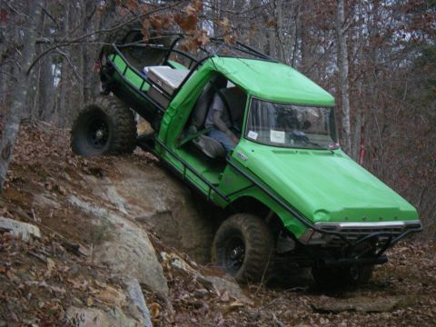 1978 Ford Bronco - This heavily modified truck is navigating a steep, rocky incline in a wooded area.