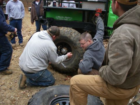 1978 Ford Bronco - Men work on a green 1978 Ford Bronco with off-road tires in a wooded area.