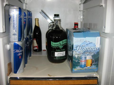 1985 Ford LTD Crown Victoria - A refrigerator stocked with various canned and bottled beverages, including beer and champagne.
