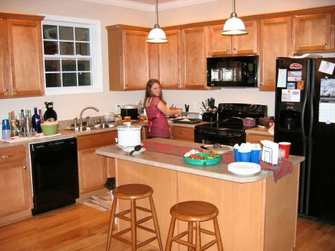 1985 Ford LTD Crown Victoria - A woman prepares food in a well-lit kitchen with a central island and two bar stools.