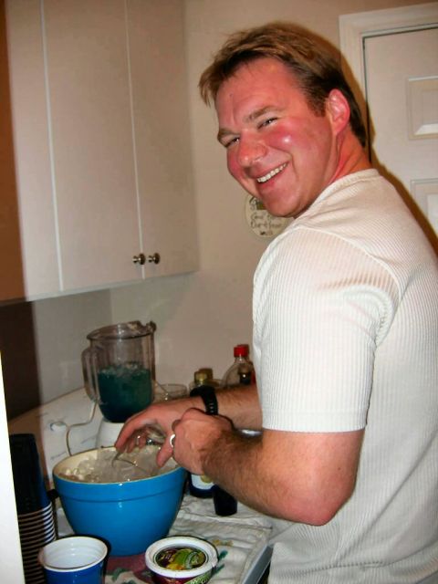 1985 Ford LTD Crown Victoria - A man smiles while preparing a beverage in a kitchen setting, with a blender and a bowl of ice visible.
