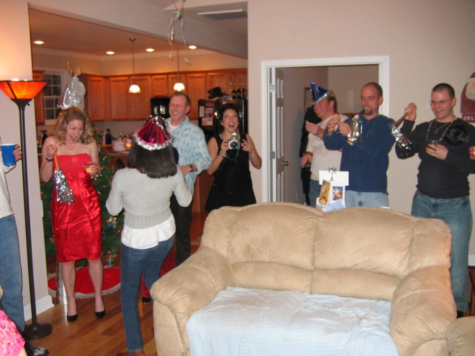 People in party hats celebrating indoors, some holding noisemakers and a camera