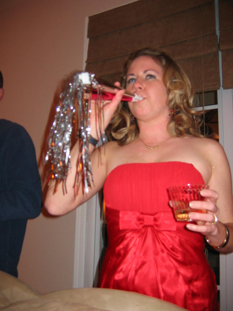 Woman in red dress blowing a party horn and holding a drink