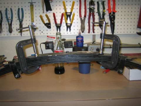 1987 Suzuki Samurai - A leaf spring suspension part is held by clamps on a workbench, with tools and supplies in the background.