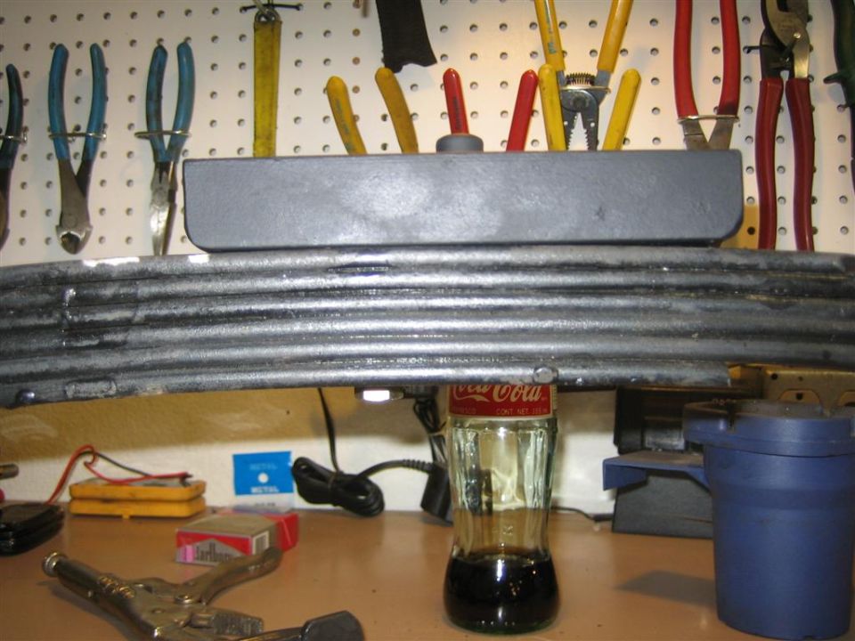 Leaf spring with a Coca-Cola bottle holding up a shock absorber, tools on pegboard behind