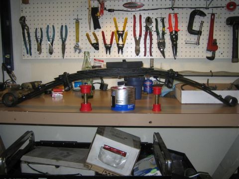 1987 Suzuki Samurai - A leaf spring suspension part, likely for a vehicle, is displayed on a workbench with tools and a can of grease.