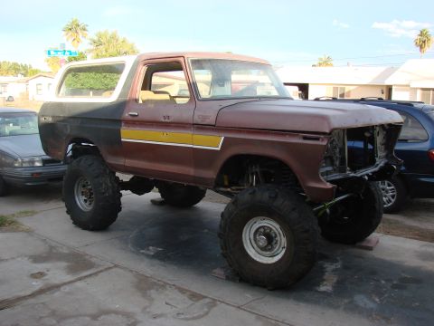 1979 Ford Bronco - This lifted Ford Bronco, missing its grille, sits on large off-road tires in a driveway.
