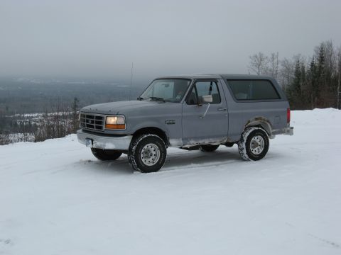 1994 Ford Bronco - A gray 1994 Ford Bronco sits on a snow-covered incline, with a distant landscape visible under an overcast sky.