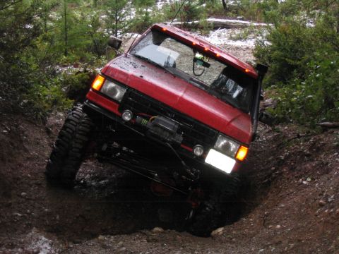 1989 Ford Bronco - Red 1989 Ford Bronco tackling a challenging off-road obstacle on a wooded trail.